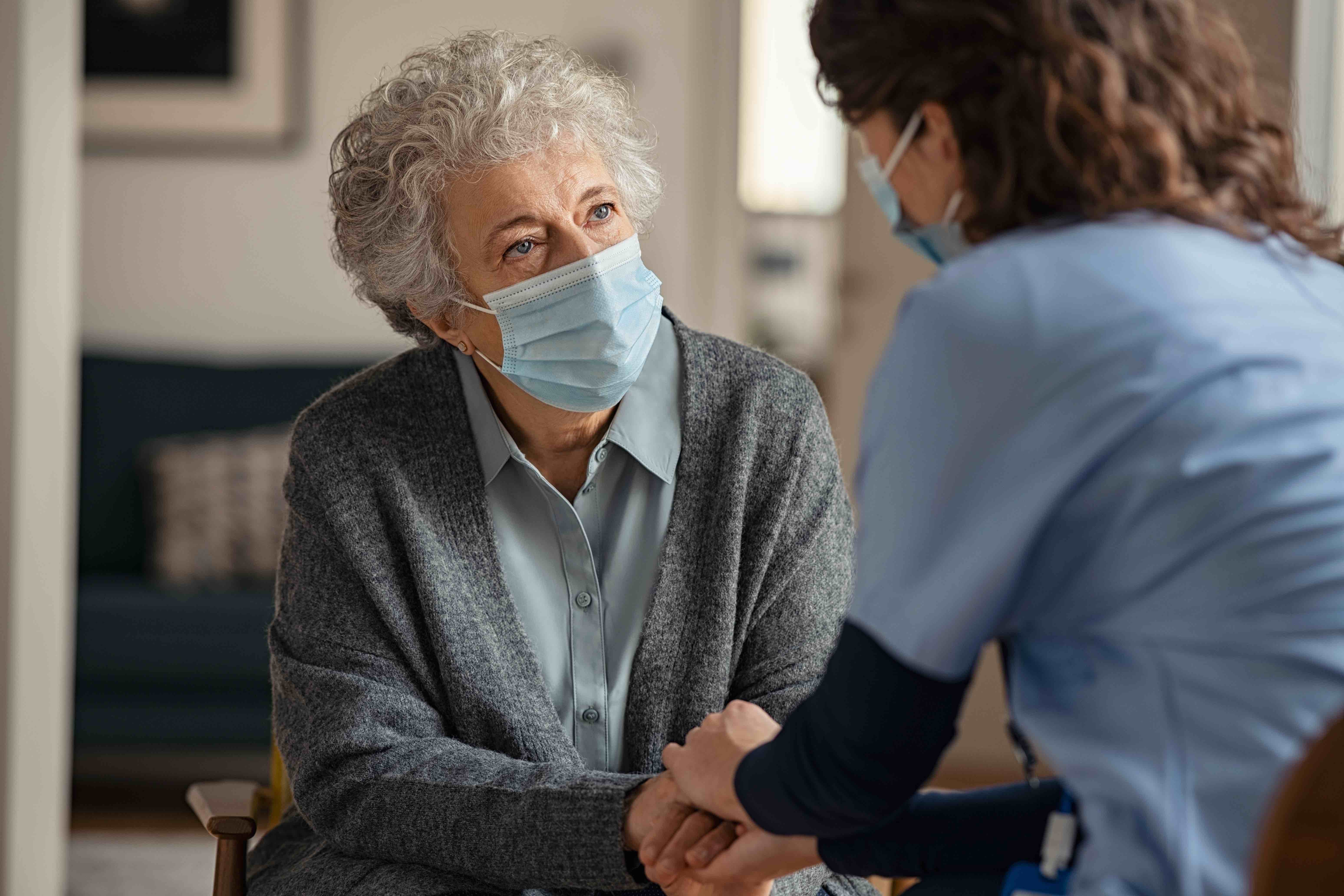 Personne âgée masquée une infirmière lui tenant la main