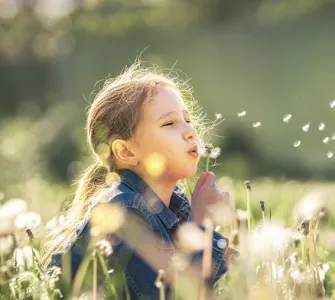 petite fille qui souffle sur un pissenlit